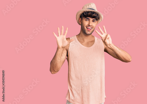 Young hispanic man wearing summer hat showing and pointing up with fingers number eight while smiling confident and happy.