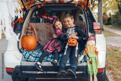 Trick or trunk. Family celebrating Halloween in trunk of car. Mother with three children kids celebrating traditional October holiday outdoors. Social distance and safe alternative celebration.