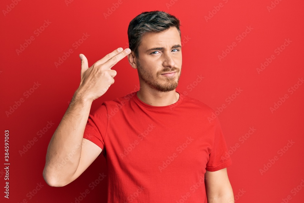 Handsome caucasian man wearing casual red tshirt shooting and killing oneself pointing hand and fingers to head like gun, suicide gesture. Handsome caucasian man wearing casual red tshirt shooting and killing oneself pointing hand and fingers to head like gun, suicide gesture.