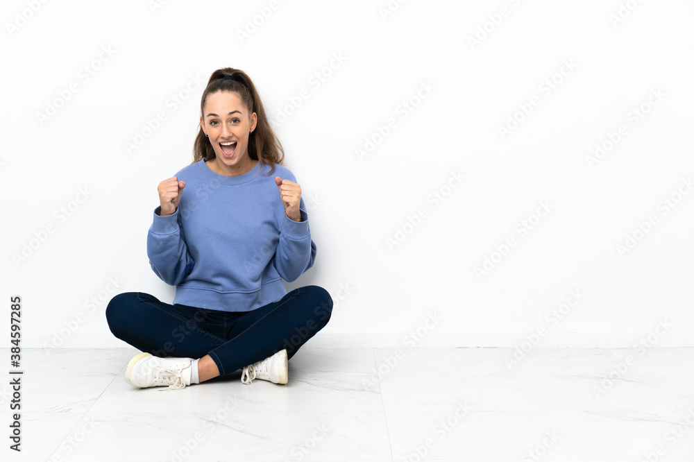Young woman sitting on the floor celebrating a victory in winner position Young woman sitting on the floor celebrating a victory in winner position