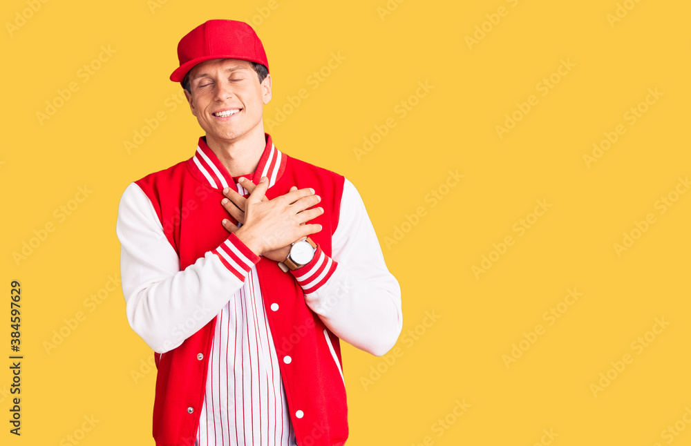 Young handsome man wearing baseball uniform smiling with hands on chest with closed eyes and grateful gesture on face. health concept. Young handsome man wearing baseball uniform smiling with hands on chest with closed eyes and grateful gesture on face. health concept.