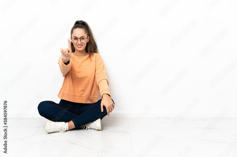 Young woman sitting on the floor showing and lifting a finger Young woman sitting on the floor showing and lifting a finger