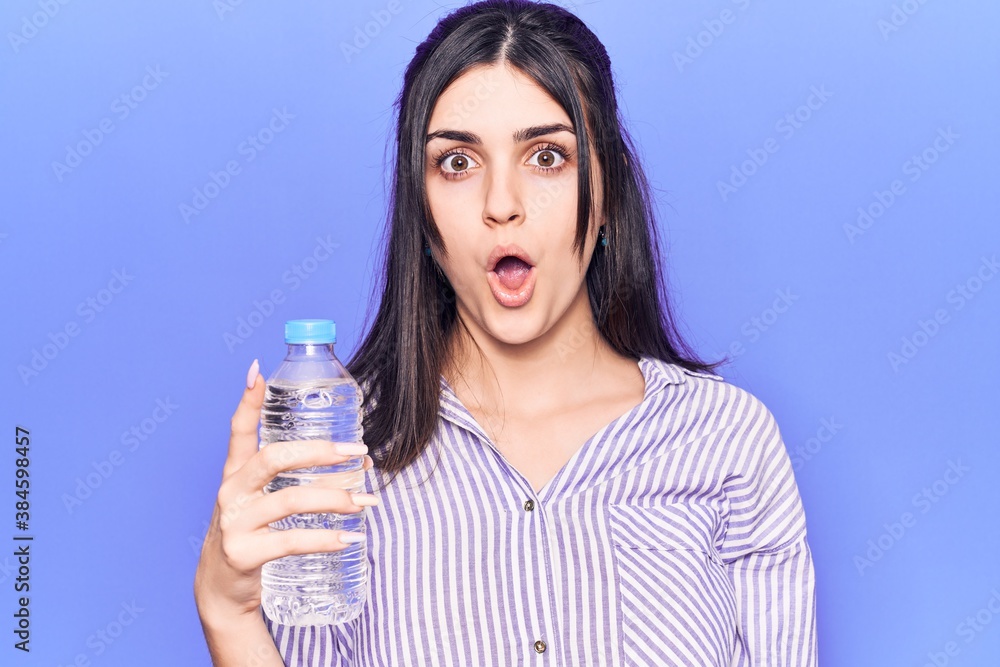Young beautiful girl holding bottle of water scared and amazed with open mouth for surprise, disbelief face Young beautiful girl holding bottle of water scared and amazed with open mouth for surprise, disbelief face