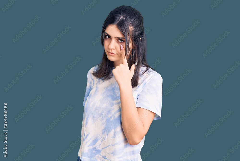 Young beautiful girl wearing casual t shirt pointing to the eye watching you gesture, suspicious expression Young beautiful girl wearing casual t shirt pointing to the eye watching you gesture, suspicious expression