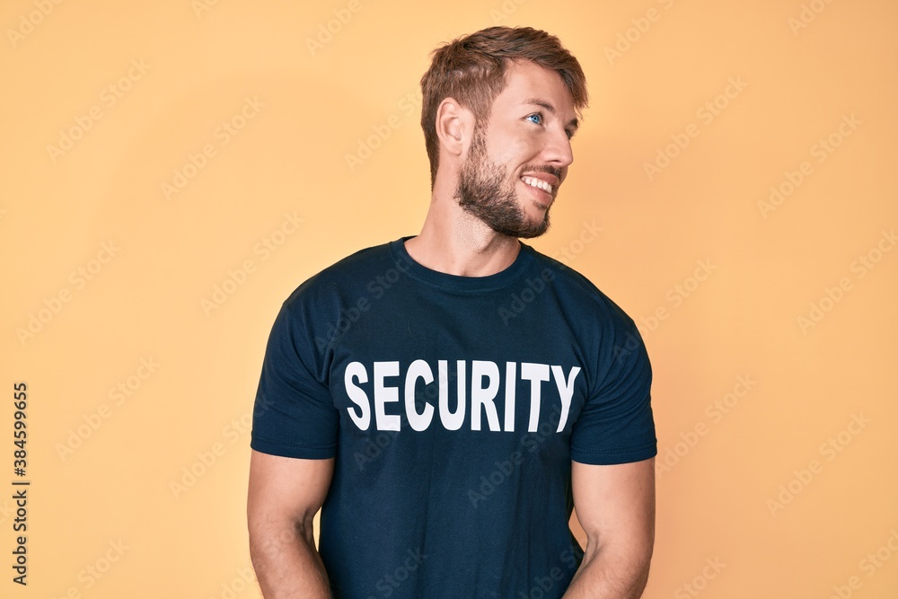 Young caucasian man wearing security t shirt looking away to side with smile on face, natural expression. laughing confident. Young caucasian man wearing security t shirt looking away to side with smile on face, natural expression. laughing confident.