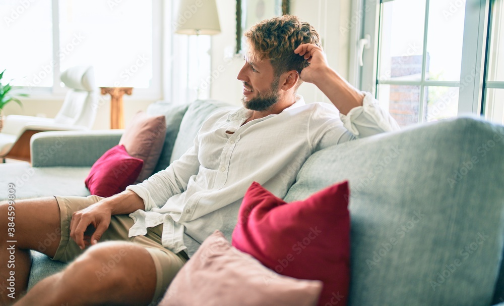 Handsome caucasian man smiling happy sitting on the sofa at home Handsome caucasian man smiling happy sitting on the sofa at home