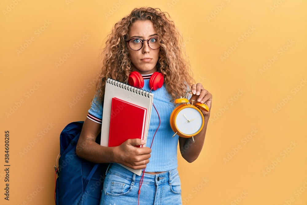 Beautiful caucasian teenager girl wearing student backpack and holding alarm clock skeptic and nervous, frowning upset because of problem. negative person. Beautiful caucasian teenager girl wearing student backpack and holding alarm clock skeptic and nervous, frowning upset because of problem. negative person.