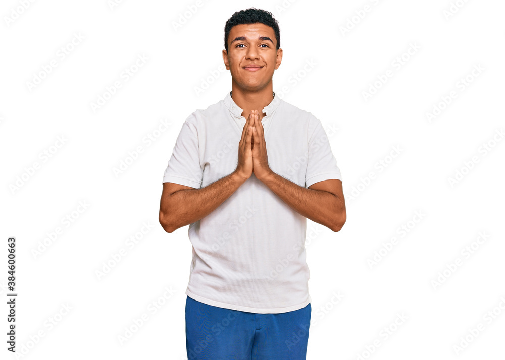 Young arab man wearing casual clothes praying with hands together asking for forgiveness smiling confident. Young arab man wearing casual clothes praying with hands together asking for forgiveness smiling confident.