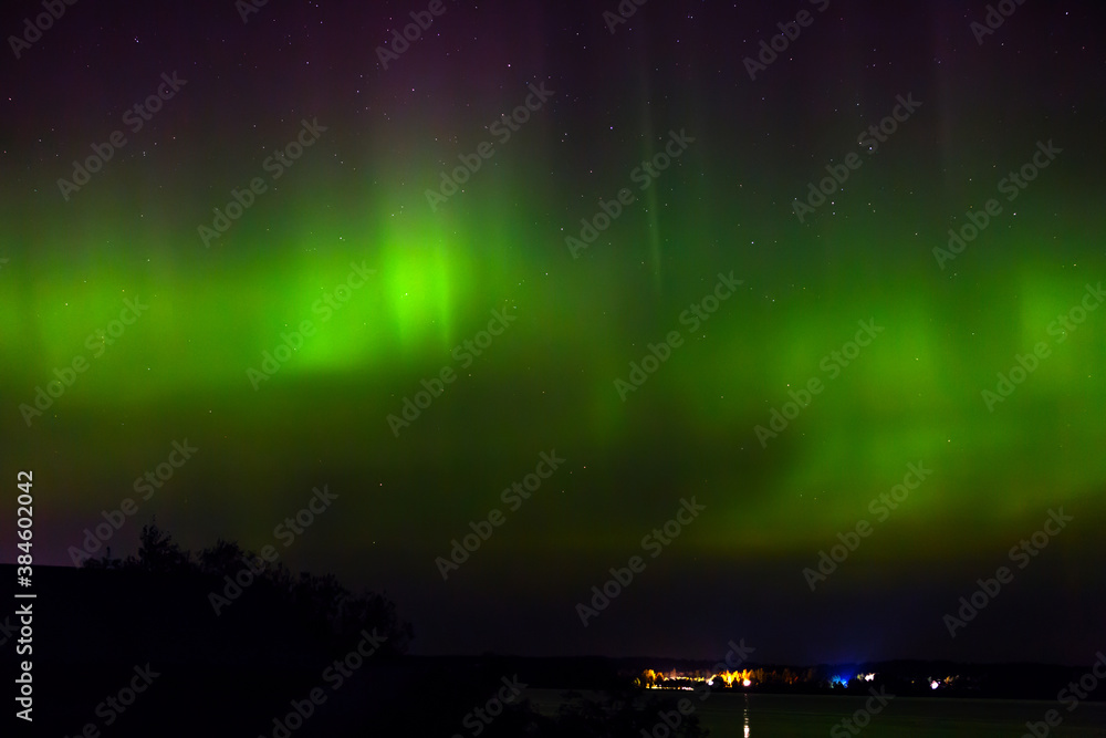 Aurora borealis over the city on the coast. Polar lights in the night starry sky over the lake.