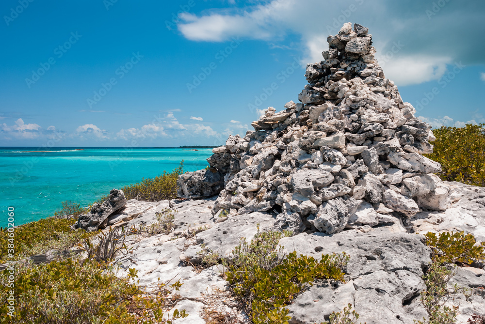 Huge white rock cairn on top of a hill overlooking the turquoise tropical ocean waters of the Exuma Islands in the Bahamas