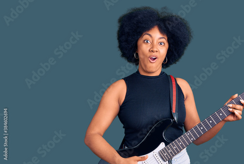 Young african american girl playing electric guitar scared and amazed with open mouth for surprise, disbelief face