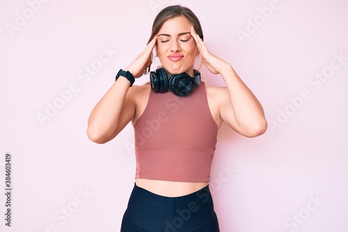 Beautiful young caucasian woman wearing gym clothes and using headphones suffering from headache desperate and stressed because pain and migraine. hands on head.