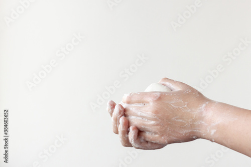 One hand on top, the other on the bottom hold the soap between the soapy palms on a white background. The concept of the need to wash hands to prevent diseases