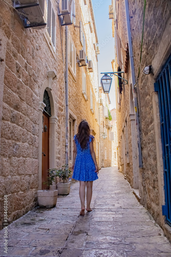 A girl in a blue dress walks along the narrow streets of the old city. Montenegro. Travel