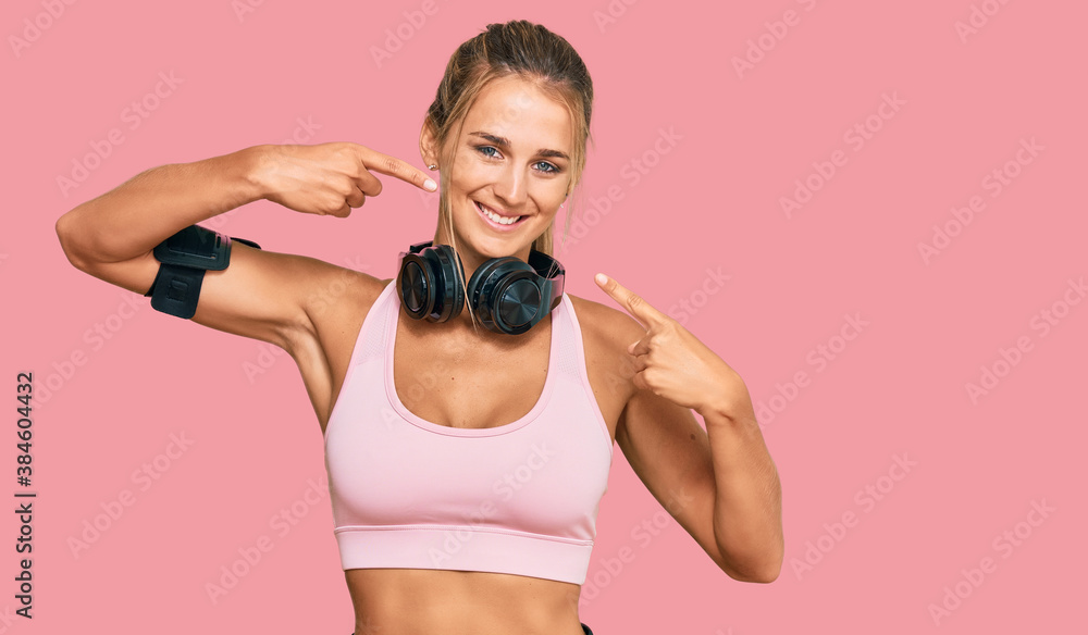 Young blonde woman wearing gym clothes and using headphones smiling cheerful showing and pointing with fingers teeth and mouth. dental health concept. Young blonde woman wearing gym clothes and using headphones smiling cheerful showing and pointing with fingers teeth and mouth. dental health concept.