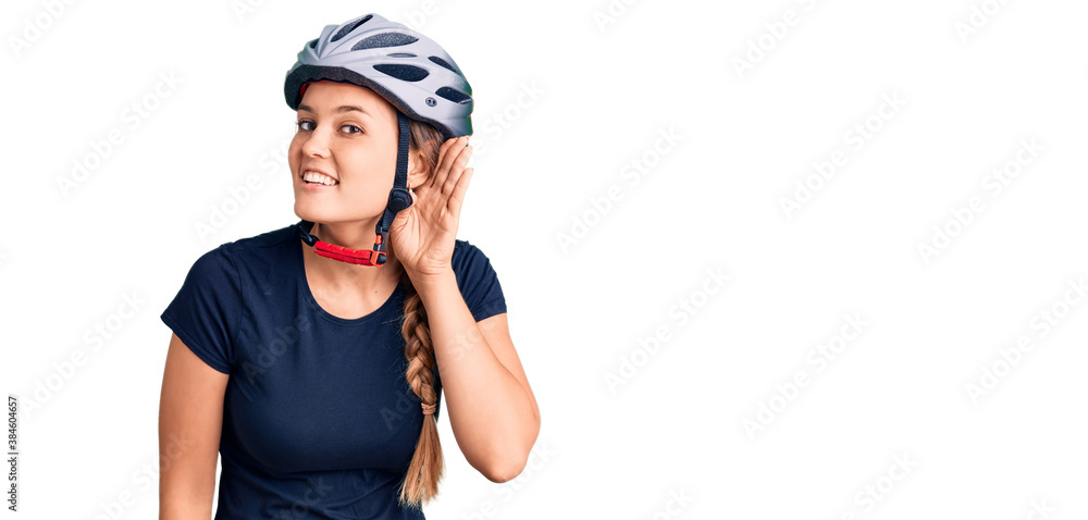 Beautiful caucasian woman wearing bike helmet smiling with hand over ear listening an hearing to rumor or gossip. deafness concept. Beautiful caucasian woman wearing bike helmet smiling with hand over ear listening an hearing to rumor or gossip. deafness concept.