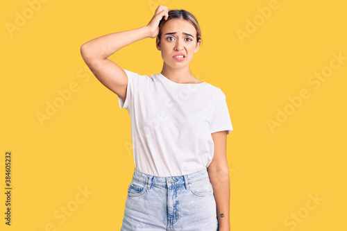 Young beautiful blonde woman wearing casual white tshirt confuse and wonder about question. uncertain with doubt, thinking with hand on head. pensive concept.