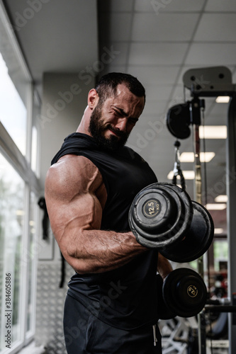 heavy bodybuilding workout motivation of strong young bearded man pumping iron lifting heavy weight dumbbells during biceps muscle training in sport gym