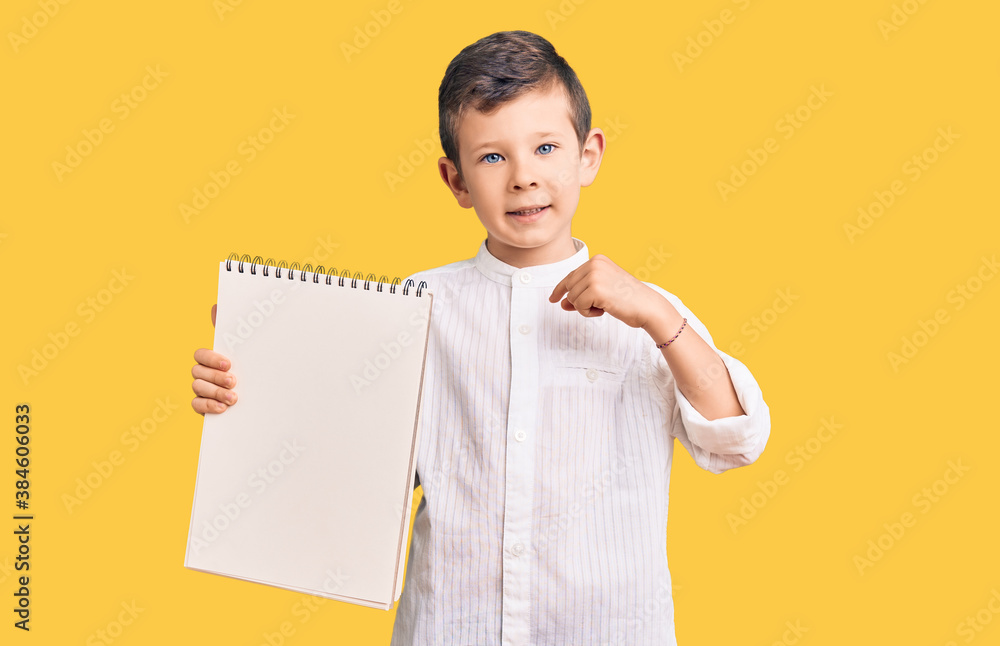 Cute blond kid holding notebook pointing finger to one self smiling happy and proud Cute blond kid holding notebook pointing finger to one self smiling happy and proud