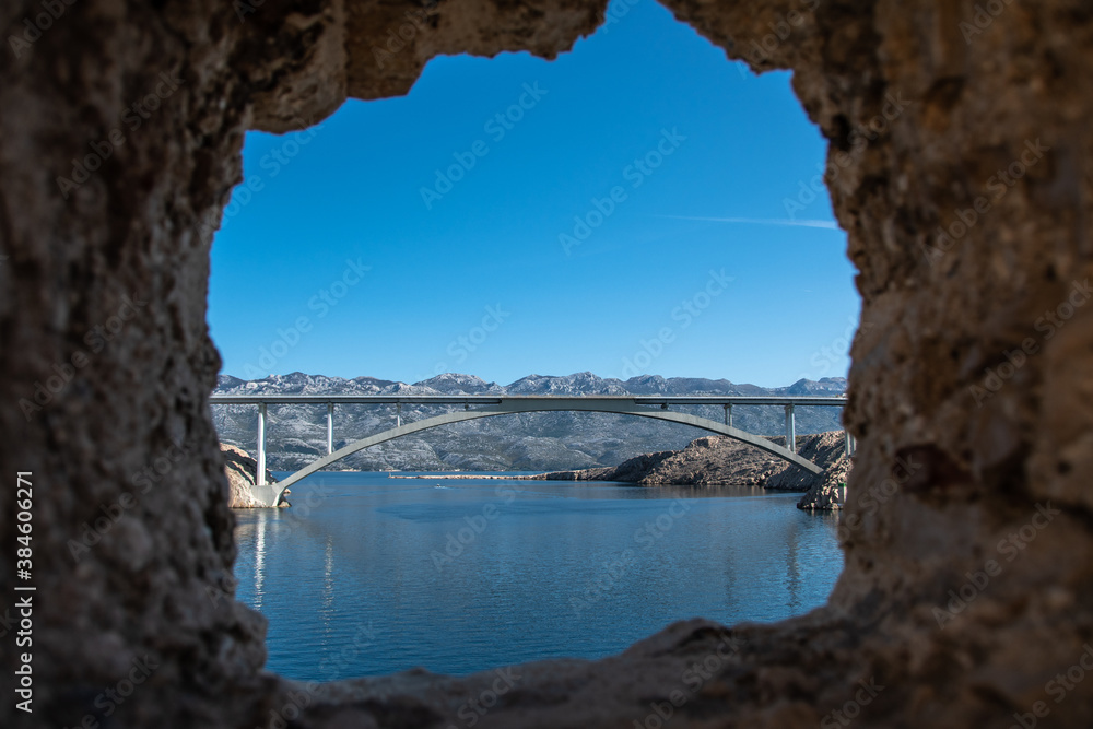 PAG ISLAND, CROATIA, 10.10.2020. Ruins of Fortica fortress and Pag bridge in distance. View through window.