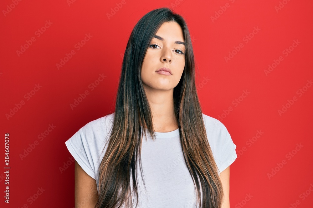 Young brunette woman wearing casual white tshirt over red background relaxed with serious expression on face. simple and natural looking at the camera. Young brunette woman wearing casual white tshirt over red background relaxed with serious expression on face. simple and natural looking at the camera.