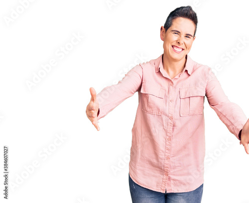 Young woman with short hair wearing casual clothes looking at the camera smiling with open arms for hug. cheerful expression embracing happiness.