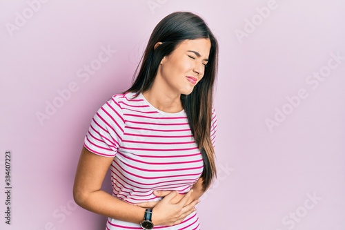 Young brunette woman wearing casual clothes over pink background with hand on stomach because indigestion, painful illness feeling unwell. ache concept. photo