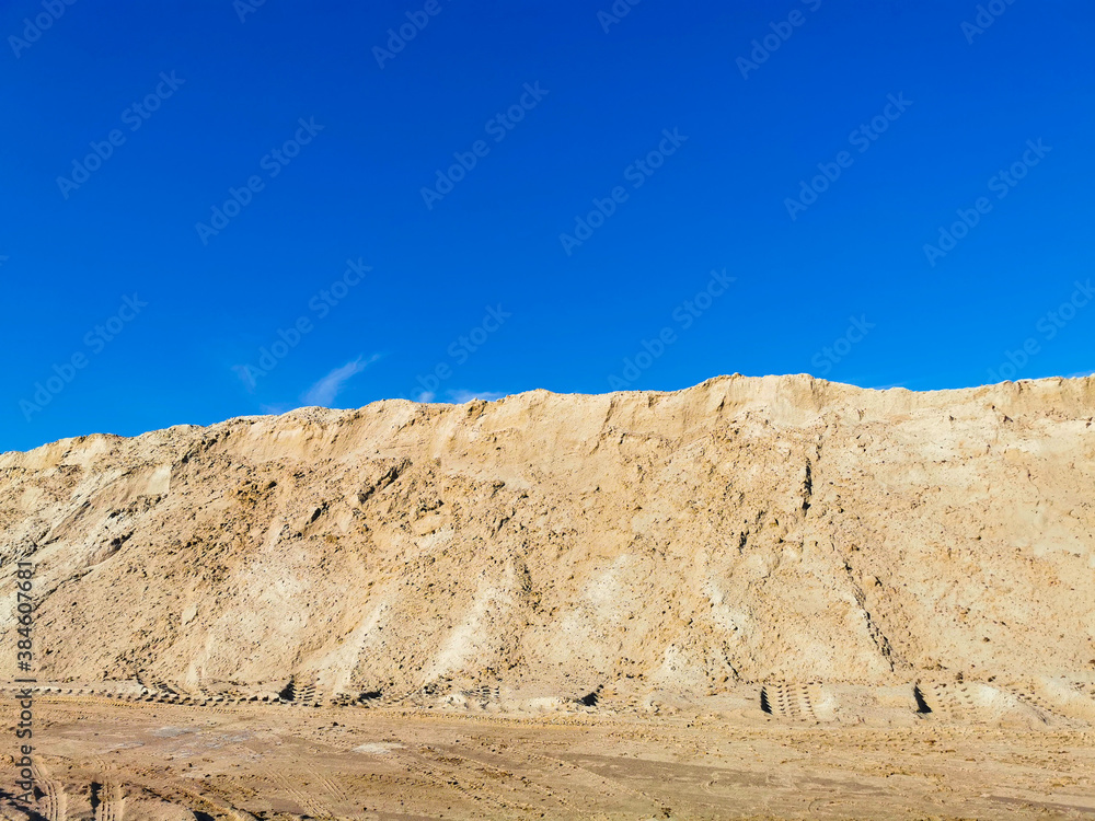 A mountain of wet yellow sand and a blue, clear sky.