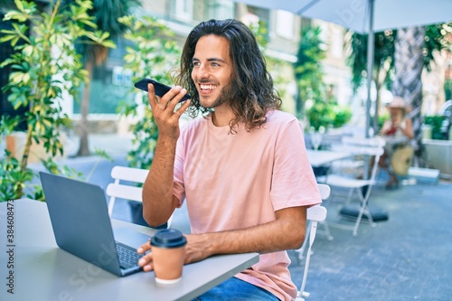 Young hispanic man smiling happy working using laptop and talking on thesmartphone at terrace of coffee shop. photo