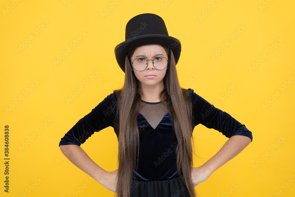 Serious female baby in glasses with long hair wear fashion party dress and hat standing with hands on hips yellow backgroud, girl Serious female baby in glasses with long hair wear fashion party dress and hat standing with hands on hips yellow backgroud, girl