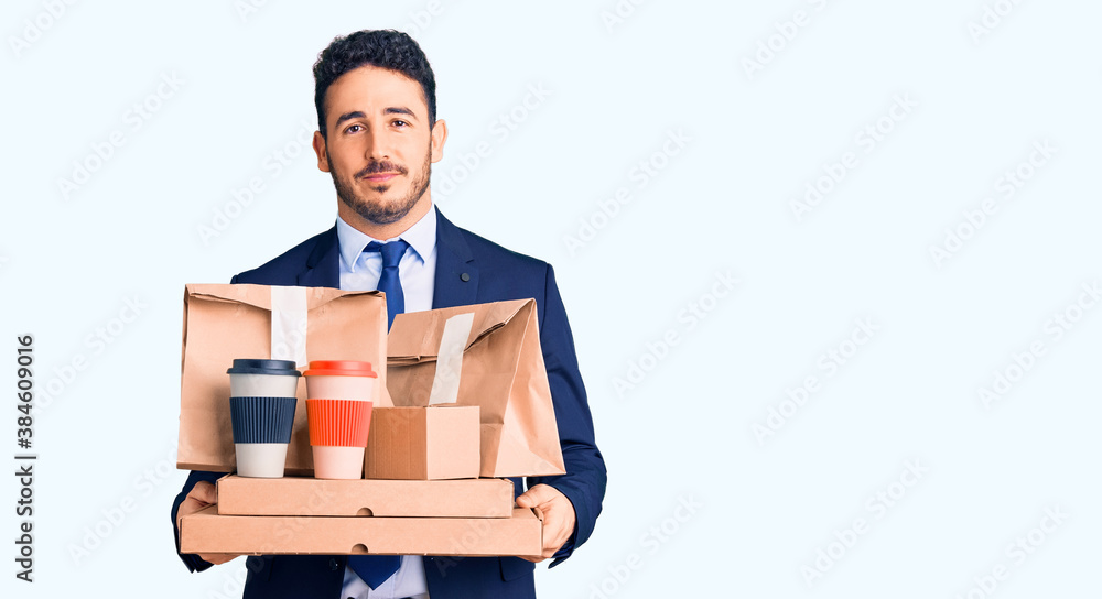 Young hispanic man wearing suit holding takeaway coffee and food thinking attitude and sober expression looking self confident Young hispanic man wearing suit holding takeaway coffee and food thinking attitude and sober expression looking self confident