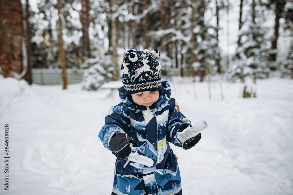 little cute caucasian boy holding icicles wearing winter overall in the countryside. Image with selective focus