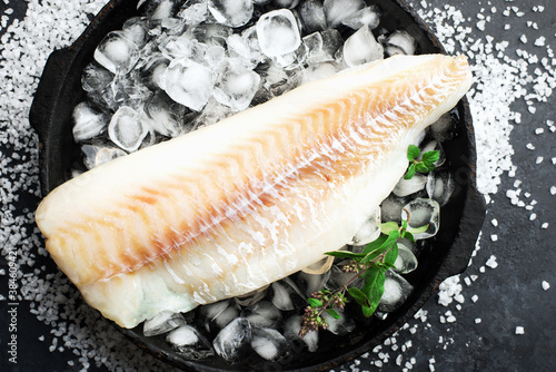 Fillet of white sea cold-water fish cod in ice cubes on a dark background. Top view