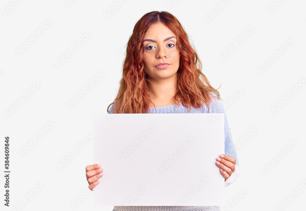 Young latin woman holding blank empty banner thinking attitude and sober expression looking self confident Young latin woman holding blank empty banner thinking attitude and sober expression looking self confident