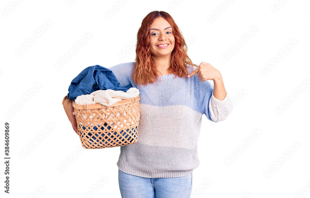 Young latin woman holding laundry basket pointing finger to one self smiling happy and proud Young latin woman holding laundry basket pointing finger to one self smiling happy and proud