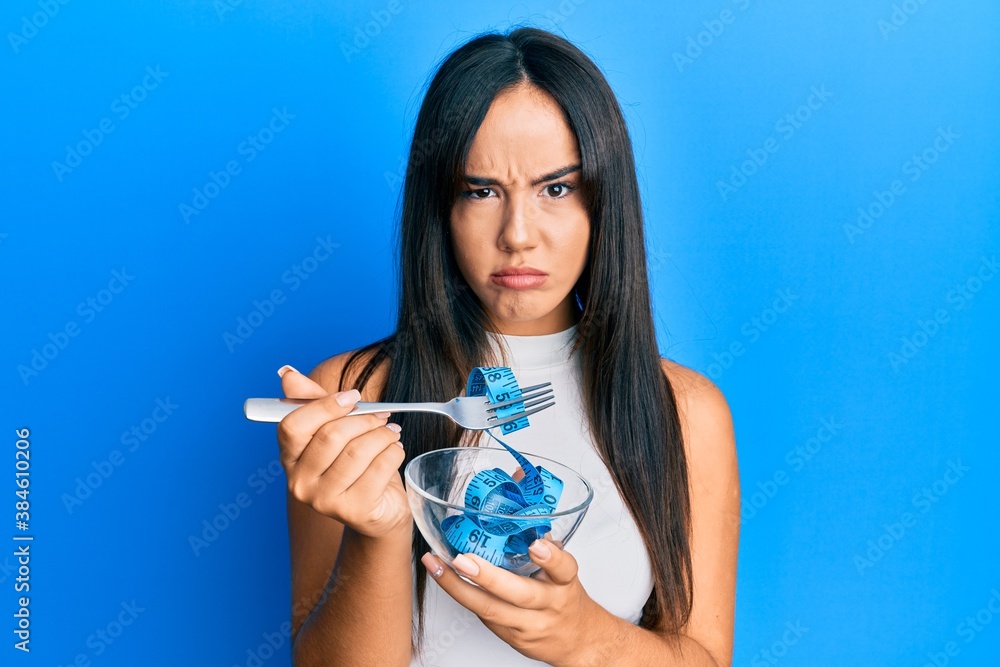 Young beautiful hispanic girl eating measure meter doing diet for weight loss skeptic and nervous, frowning upset because of problem. negative person. Young beautiful hispanic girl eating measure meter doing diet for weight loss skeptic and nervous, frowning upset because of problem. negative person.