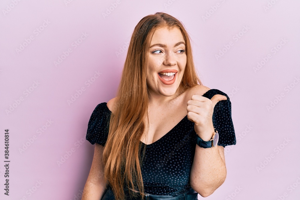 Young beautiful redhead woman wearing elegant and sexy look pointing thumb up to the side smiling happy with open mouth Young beautiful redhead woman wearing elegant and sexy look pointing thumb up to the side smiling happy with open mouth
