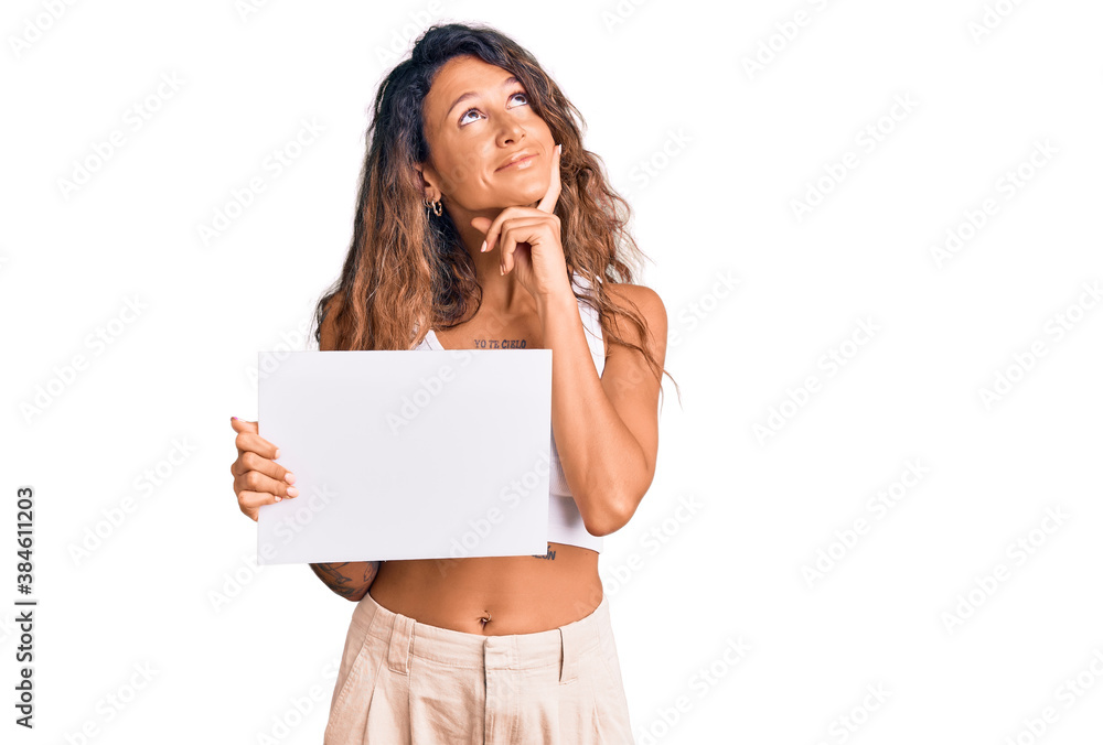 Young hispanic woman with tattoo holding blank empty paper serious face thinking about question with hand on chin, thoughtful about confusing idea Young hispanic woman with tattoo holding blank empty paper serious face thinking about question with hand on chin, thoughtful about confusing idea