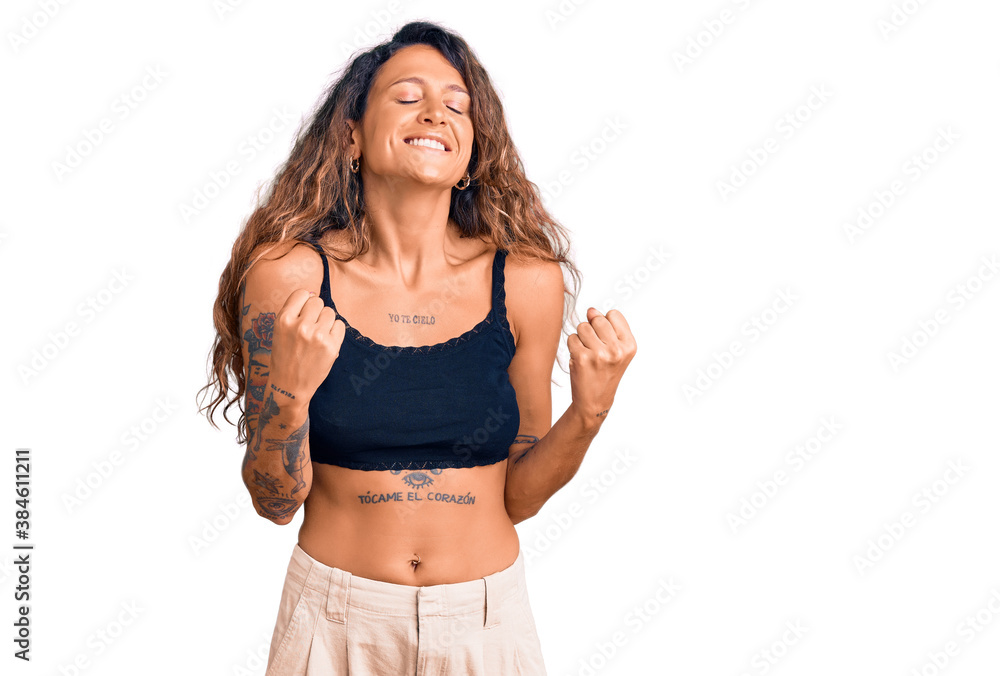 Young hispanic woman with tattoo wearing casual clothes excited for success with arms raised and eyes closed celebrating victory smiling. winner concept. Young hispanic woman with tattoo wearing casual clothes excited for success with arms raised and eyes closed celebrating victory smiling. winner concept.
