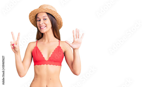 Beautiful brunette young woman wearing bikini showing and pointing up with fingers number seven while smiling confident and happy.