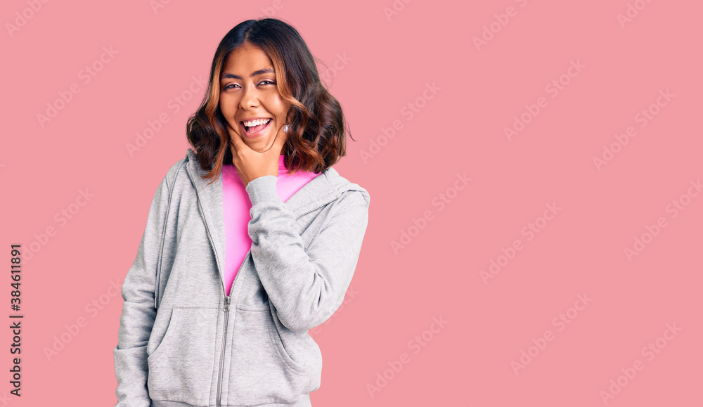 Young beautiful mixed race woman wearing casual sporty clothes looking confident at the camera smiling with crossed arms and hand raised on chin. thinking positive. Young beautiful mixed race woman wearing casual sporty clothes looking confident at the camera smiling with crossed arms and hand raised on chin. thinking positive.