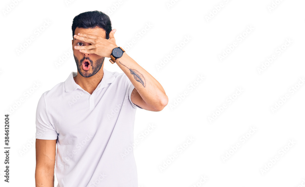 Fototapeta premium Young handsome hispanic man wearing casual clothes peeking in shock covering face and eyes with hand, looking through fingers with embarrassed expression.