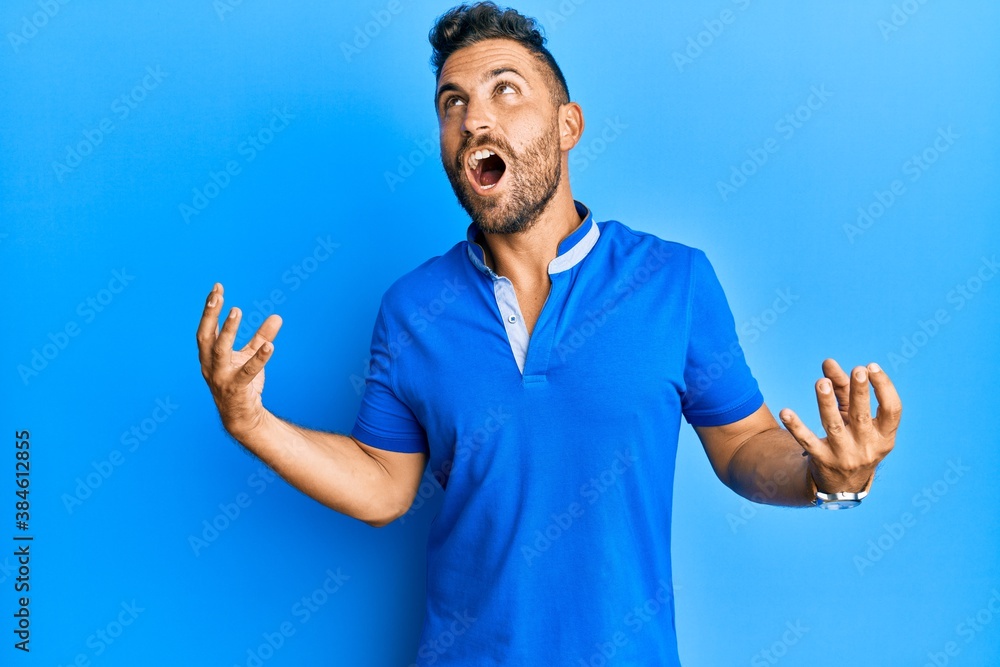 Handsome man with beard wearing casual clothes crazy and mad shouting and yelling with aggressive expression and arms raised. frustration concept. Handsome man with beard wearing casual clothes crazy and mad shouting and yelling with aggressive expression and arms raised. frustration concept.
