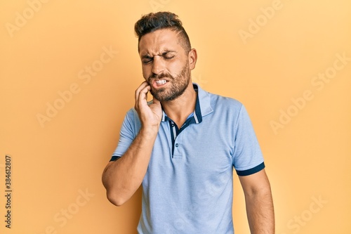 Handsome man with beard wearing casual clothes touching mouth with hand with painful expression because of toothache or dental illness on teeth. dentist