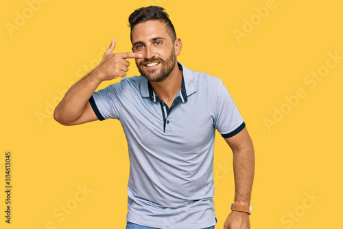 Handsome man with beard wearing casual clothes pointing with hand finger to face and nose, smiling cheerful. beauty concept