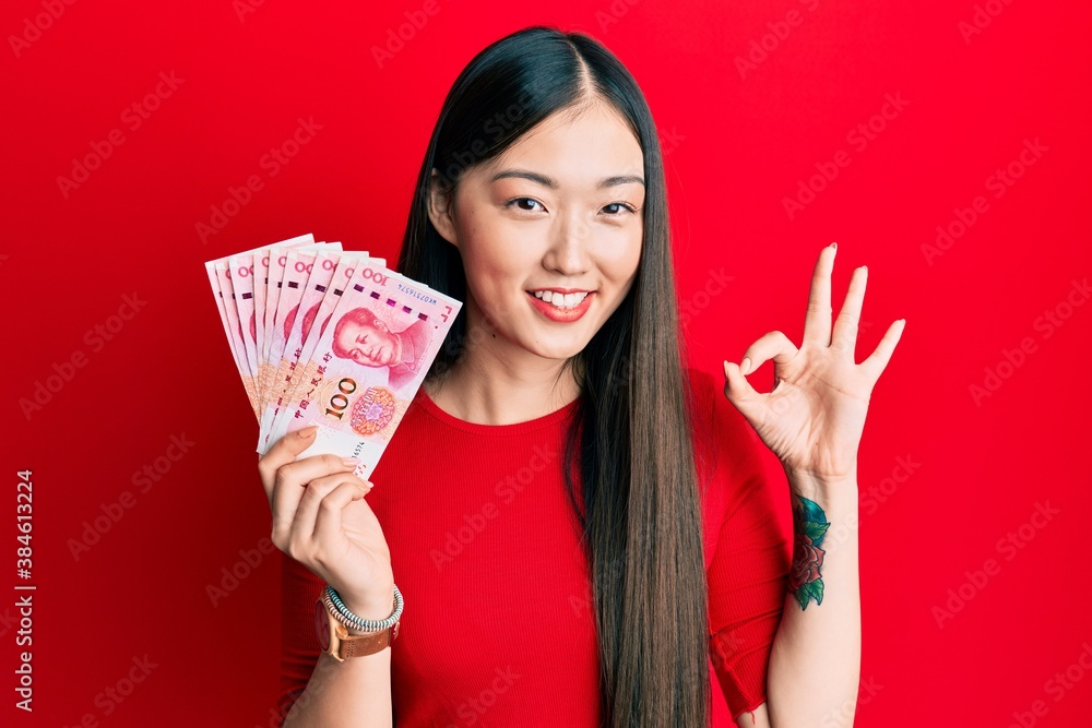 Young chinese woman holding 10 yuan chinese banknotes doing ok sign with fingers, smiling friendly gesturing excellent symbol Young chinese woman holding 10 yuan chinese banknotes doing ok sign with fingers, smiling friendly gesturing excellent symbol