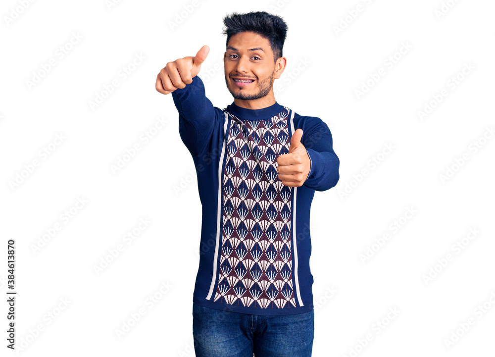 Handsome latin american young man wearing casual winter sweater approving doing positive gesture with hand, thumbs up smiling and happy for success. winner gesture. Handsome latin american young man wearing casual winter sweater approving doing positive gesture with hand, thumbs up smiling and happy for success. winner gesture.
