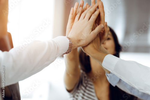Group of business people joining hands or giving five to each other after meeting or negotiation in sunny office