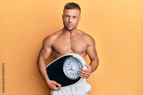 Handsome muscle man holding weight machine to balance weight loss skeptic and nervous  frowning upset because of problem. negative person.