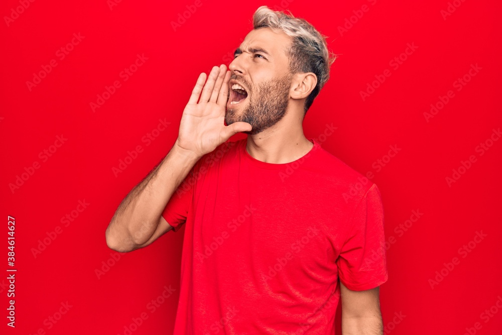 Young handsome blond man wearing casual red t-shirt standing over isolated red background shouting and screaming loud to side with hand on mouth. Communication concept. Young handsome blond man wearing casual red t-shirt standing over isolated red background shouting and screaming loud to side with hand on mouth. Communication concept.